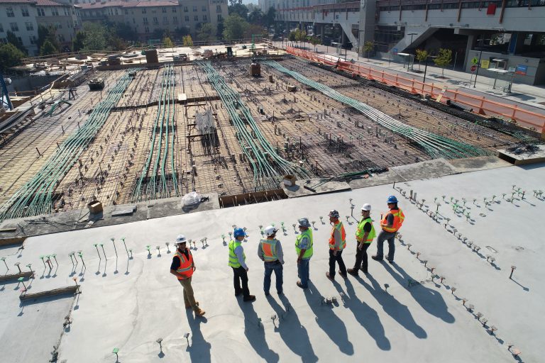 Several construction workers gathered on a construction site, wearing safety gear and discussing their tasks.